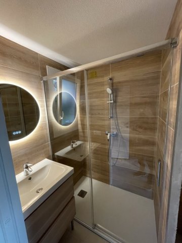 Rénovation moderne et élégante d'une salle de bain avec douche à l'italienne transparente, meuble vasque suspendu en bois, et miroir LED circulaire par Al'eau Nico et Eau Secours