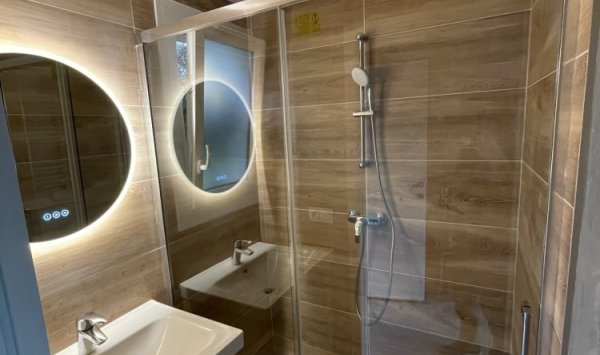 Rénovation moderne et élégante d'une salle de bain avec douche à l'italienne transparente, meuble vasque suspendu en bois, et miroir LED circulaire par Al'eau Nico et Eau Secours